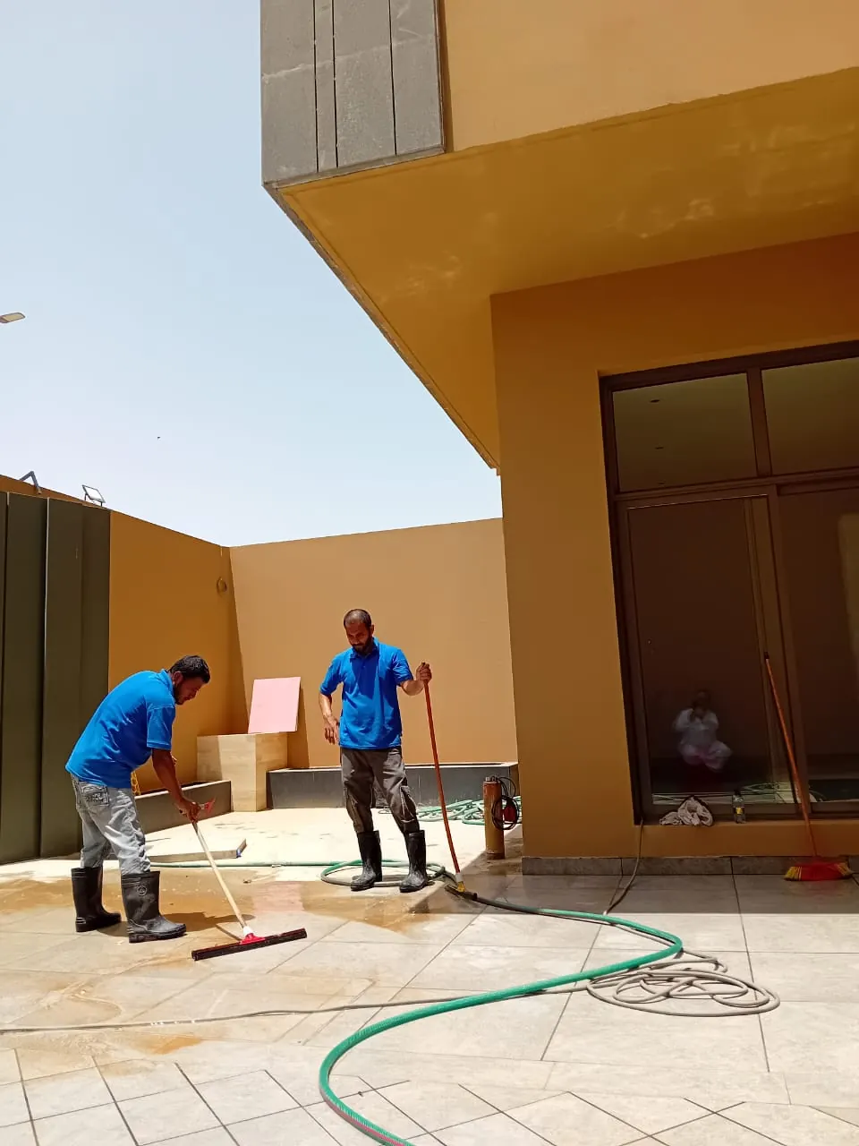 عاملان يفركان أرضية فناء خارجي بجانب مبنى سكني