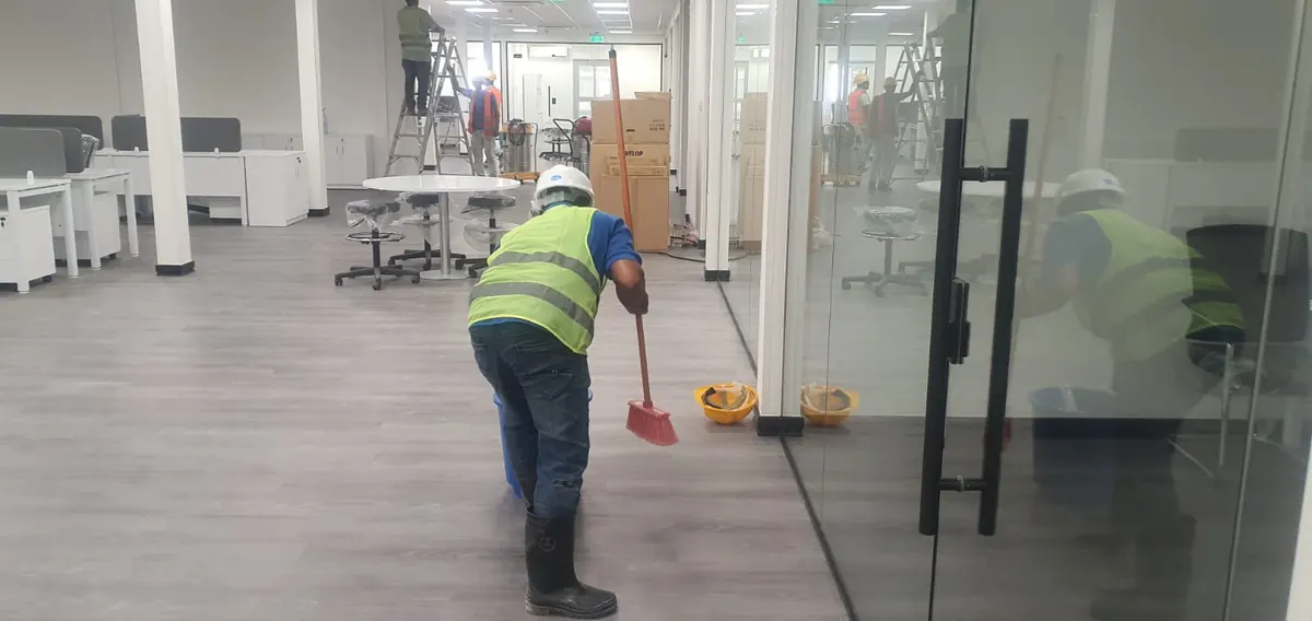 عامل يكنس أرضية مكتب جديد بينما يعمل آخرون على سلالم في الخلف